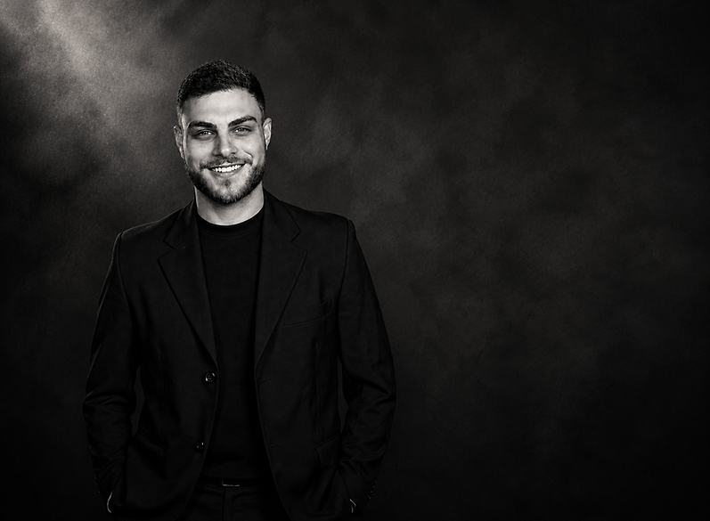 Thiago vestindo blaser, sorrindo, fundo escuro com fumaça e foto em preto e branco