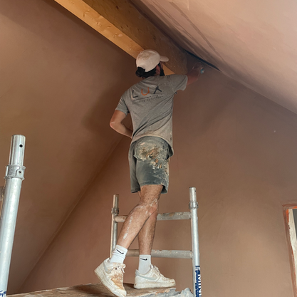 Construction worker plastering a ceiling while standing on a ladder in the attic.