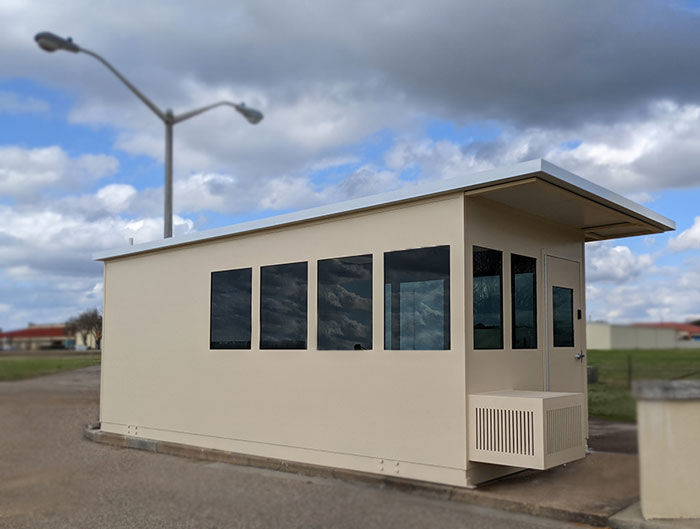 beige security booth with large windows and a door, equipped with an air conditioning unit for climate control.
