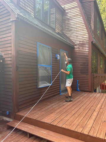 Aaron is spraying paint brown stain for an exterior painting project in Andover CT