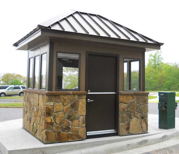 security booth with a stone base and a metal roof, featuring windows and a door for access control and monitoring.