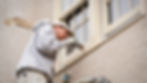 homeowner on a ladder painting the exterior window frames of his home