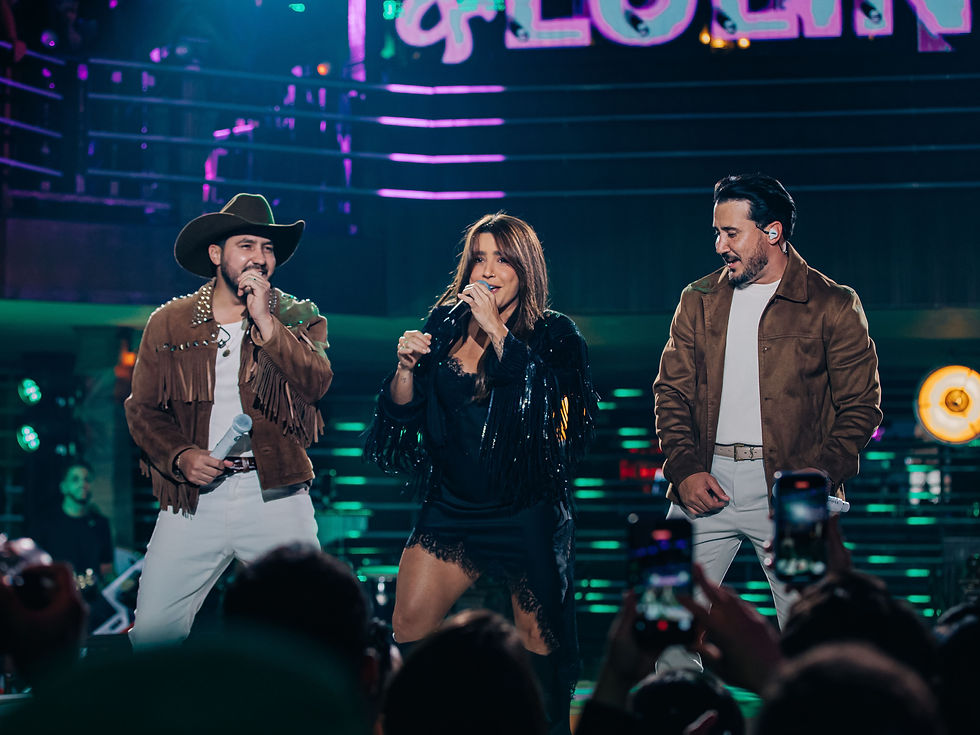 Iguinho e Lulinha posam ao lado de Lauana Prado no palco do Villa Country. A dupla sorri enquanto segura microfones, e Lauana aparece ao centro, iluminada pelas luzes cênicas do DVD “Abre a Porteira”. O cenário tem tons quentes e elementos que remetem ao forró e ao piseiro.