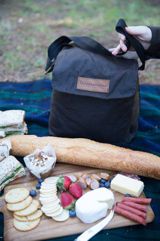 A Didgeridoona lunch bag and fruit and cheese board setup on a picnic blanket.