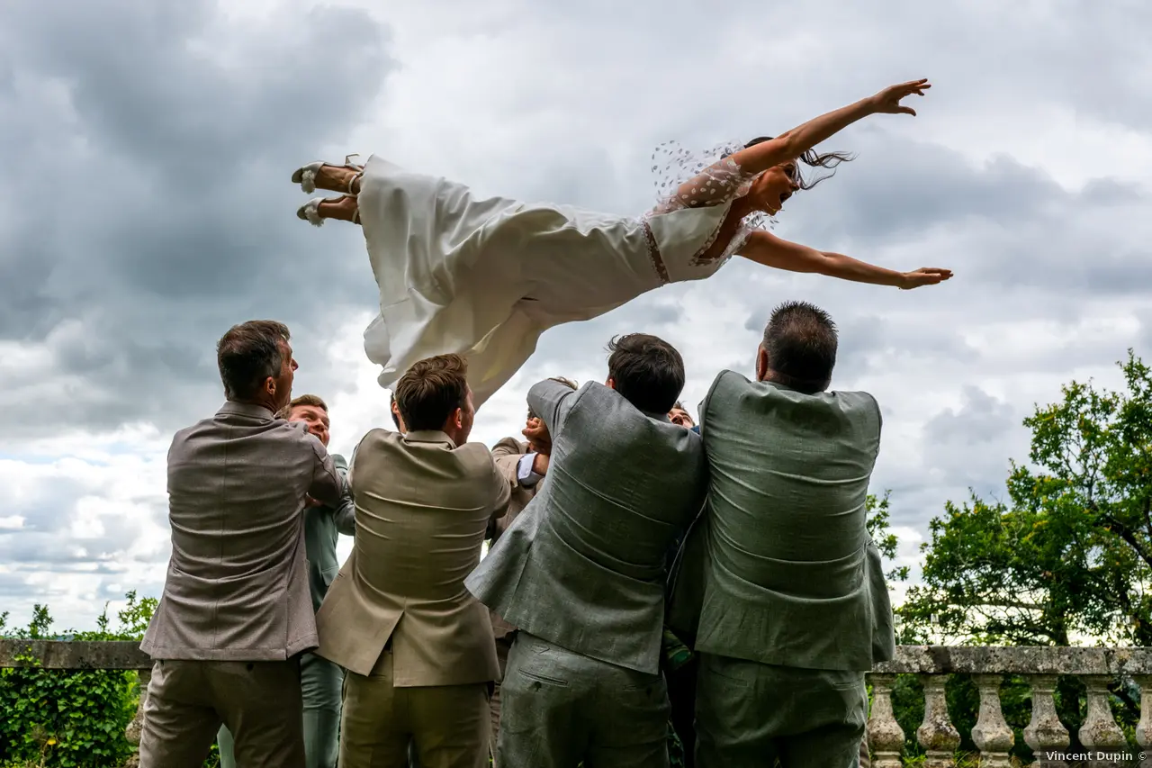 la mariée est lancée dans les airs comme une danseuse bras en avant par un groupe de 8 garçons d'honneur