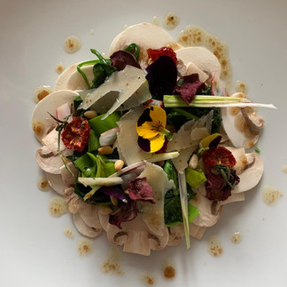 Mushroom carpaccio with cep mushroom jus and crunchy vegetables in shades of white, green, red, and yellow. All arranged in a circular pattern.