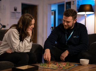 Residential childcare worker supporting a young person during a calm evening activity inside a children’s residential home in Crewe, with warm low lighting and a relaxed communal environment.