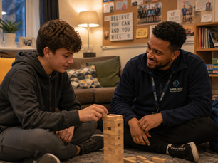 Residential support worker playing Jenga with a young person in a warm Nottingham children’s residential home lounge during an evening activity session.