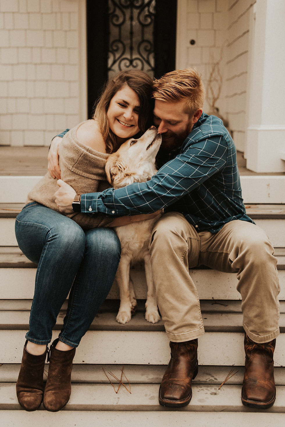 couple giving their dog a hug in front of their house