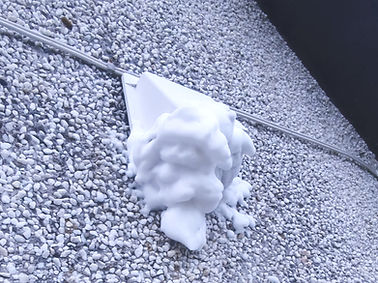 A hole in the ground filled with snow and rocks, revealing a wasp nest inside covered by foam, located in East Lothian.