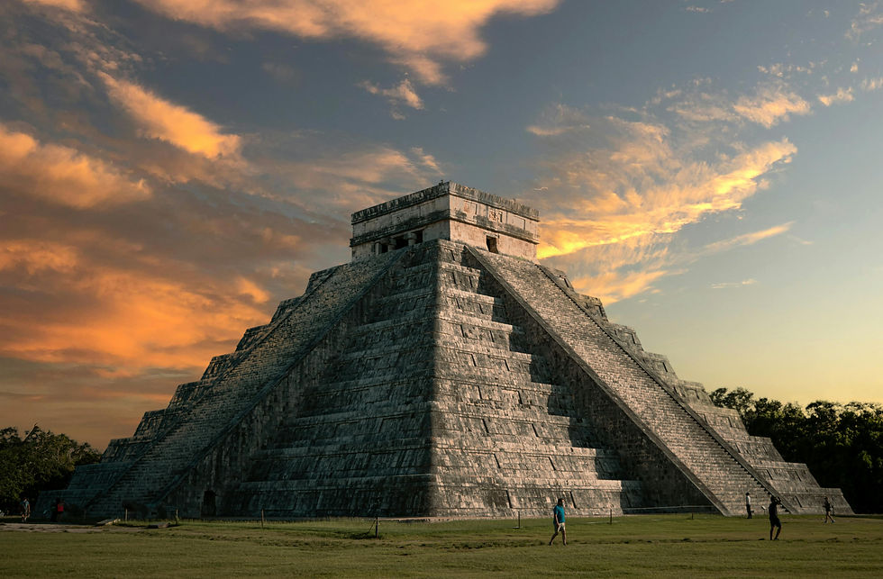 People walk near a Chichen Itza under a vibrant sunset sky, with orange clouds. The mood is serene and historical.