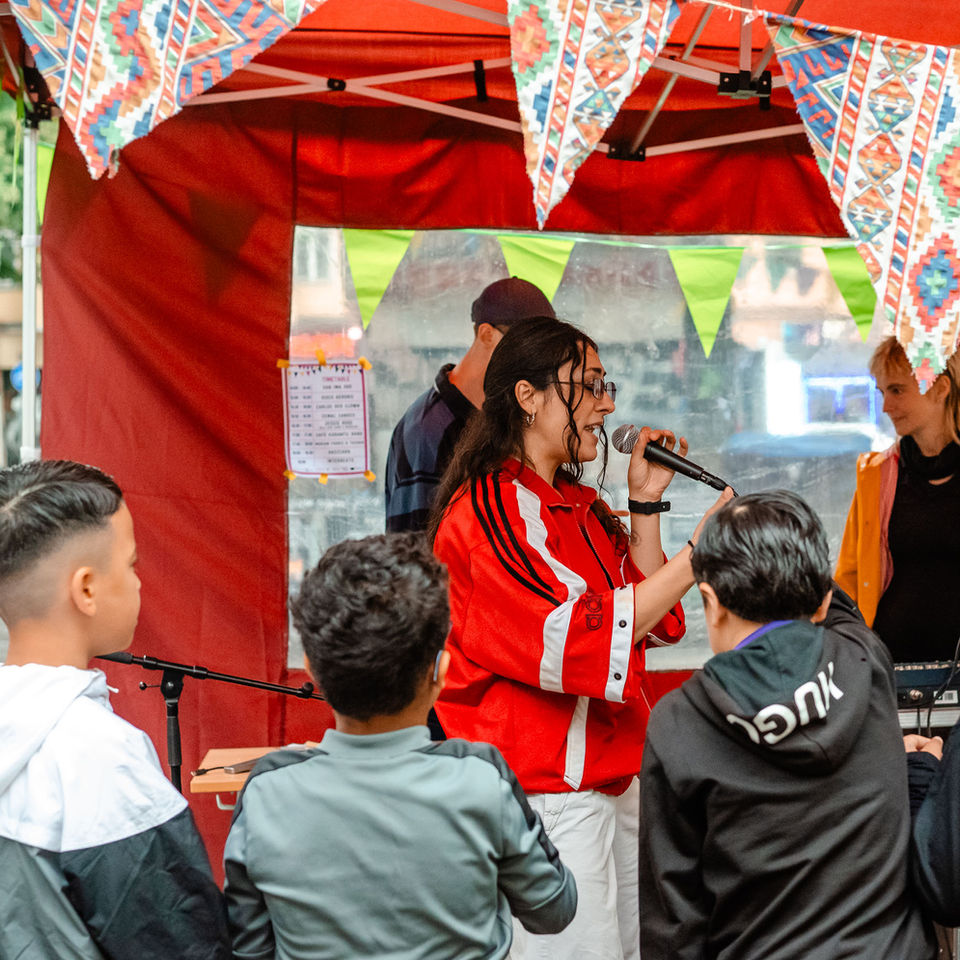 Im Vordergrund sind vier Jungs von hinten zu sehen, die einer Rapperin auf der Bühne zuschauen. 