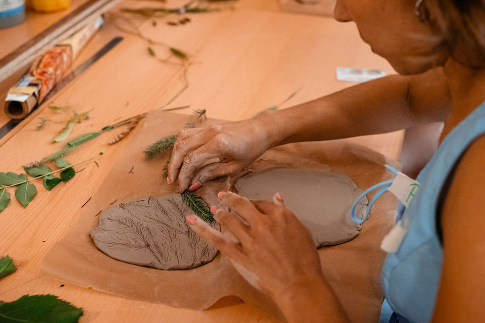 Ausgerollte Keramikmasse und zwei Hände, die einen Zweig in den Ton drücken