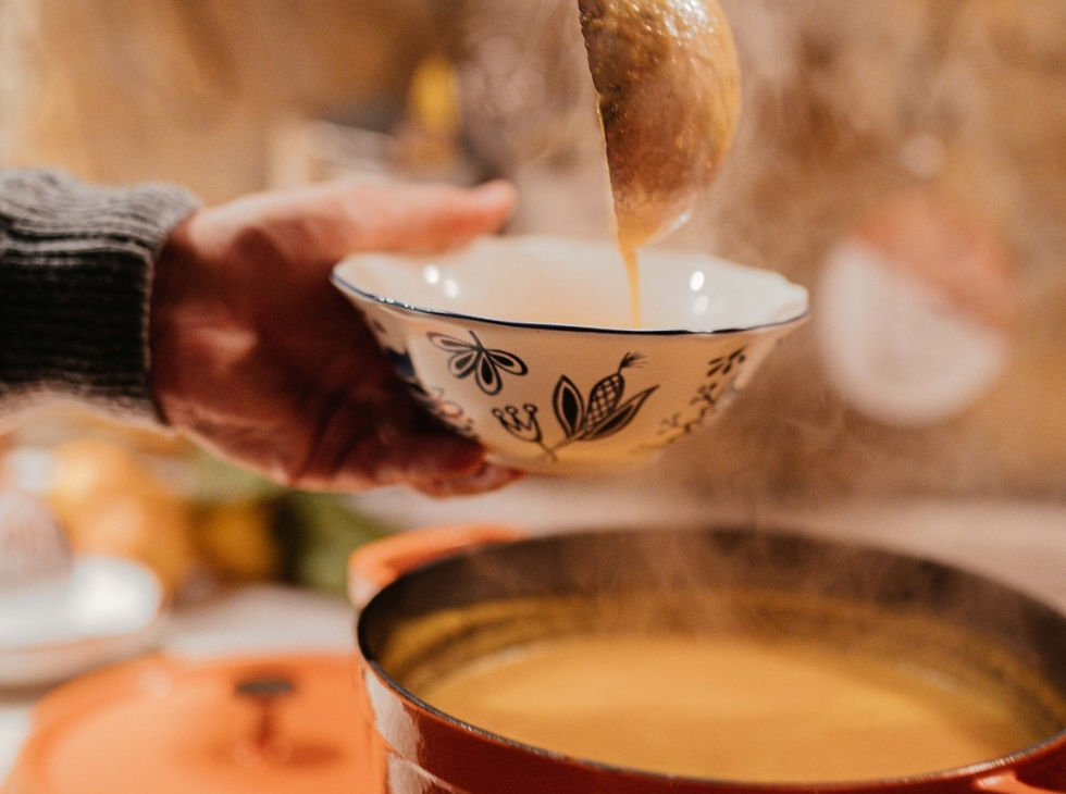 Hand holds patterned bowl as steaming soup is ladled from a pot in a warm kitchen scene
