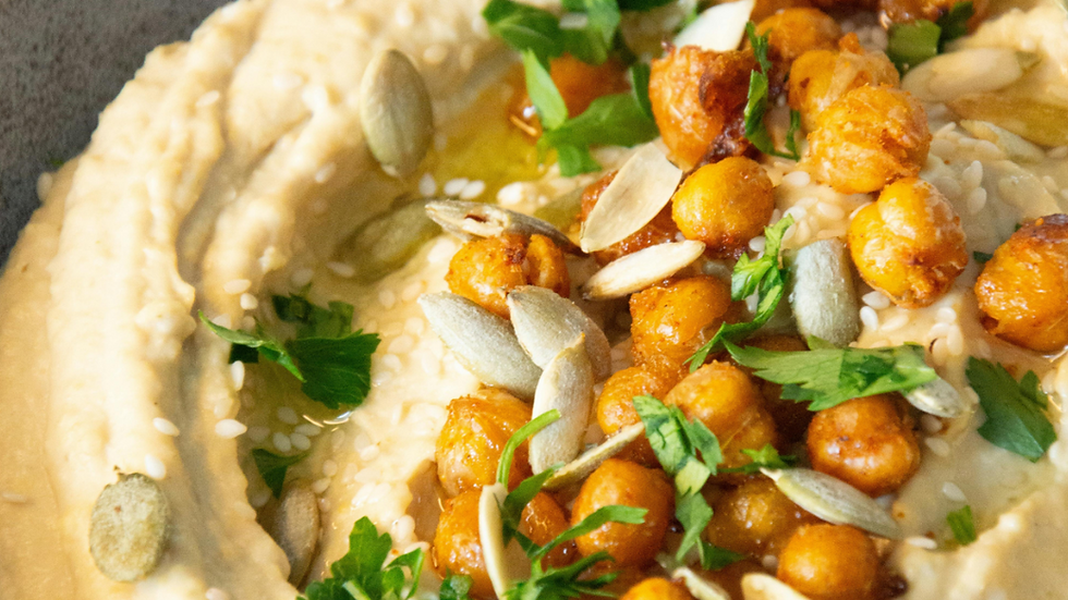 Creamy hummus topped with roasted chickpeas, pumpkin seeds, sesame seeds, and fresh parsley. The colors are warm and inviting.