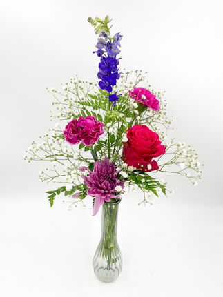 Jewel tone bud vase with a lavender cremone, hot pink rose, novelty carnations, and purple larkspur accented with baby's breath and greenery.