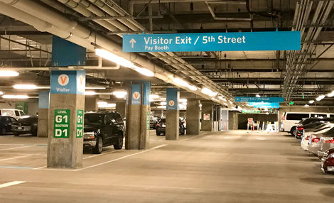 View of underground parking garage area with new blue signage painted on support columns and suspended signage above vehicle traffic lanes.