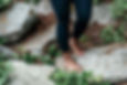 An image of an African American Woman wearing black tights in her bare feet walking across boulders. Grounding