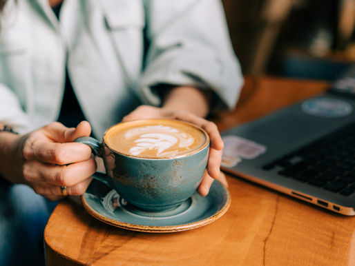 Person holding coffee cup at table with a laptop next to them