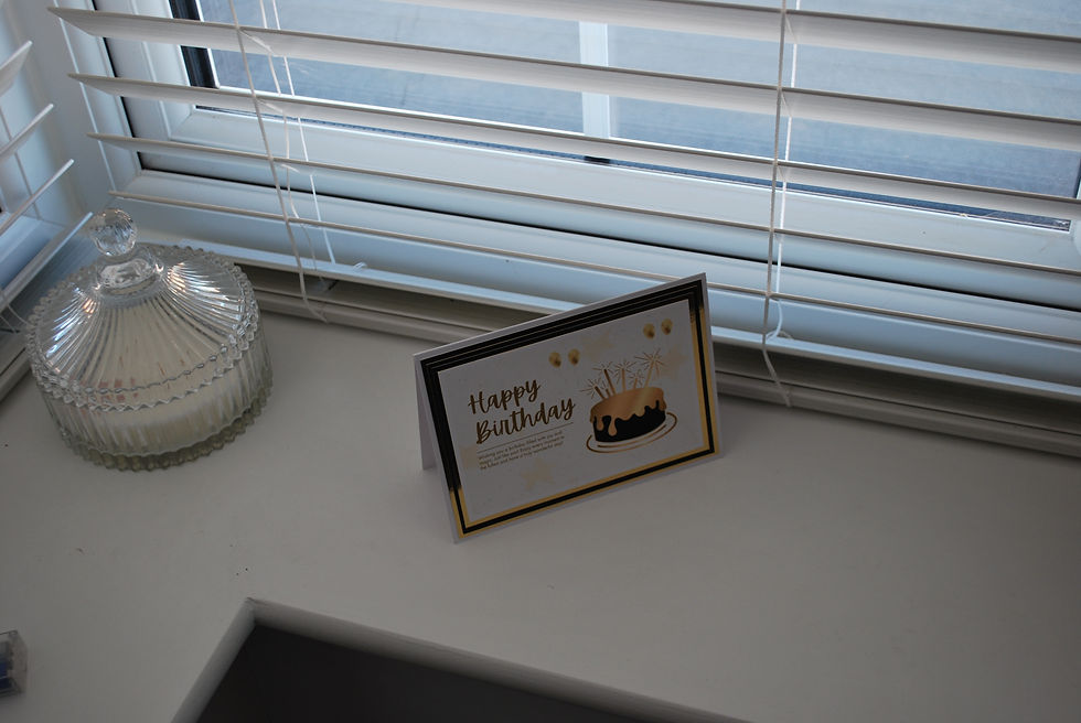 Thumbnail: Gold and black "Happy Birthday" card standing on a white windowsill next to a glass candle jar.
