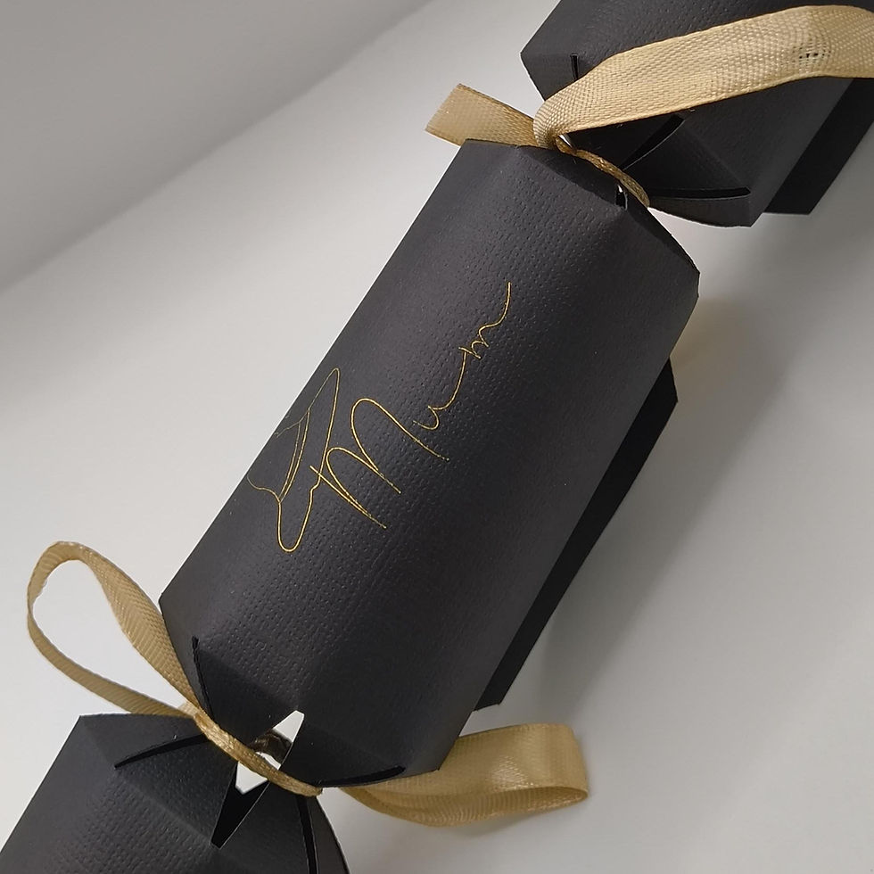 Assembled black cracker with gold “Mum” lettering and gold ribbon bows, shown on light backdrop.