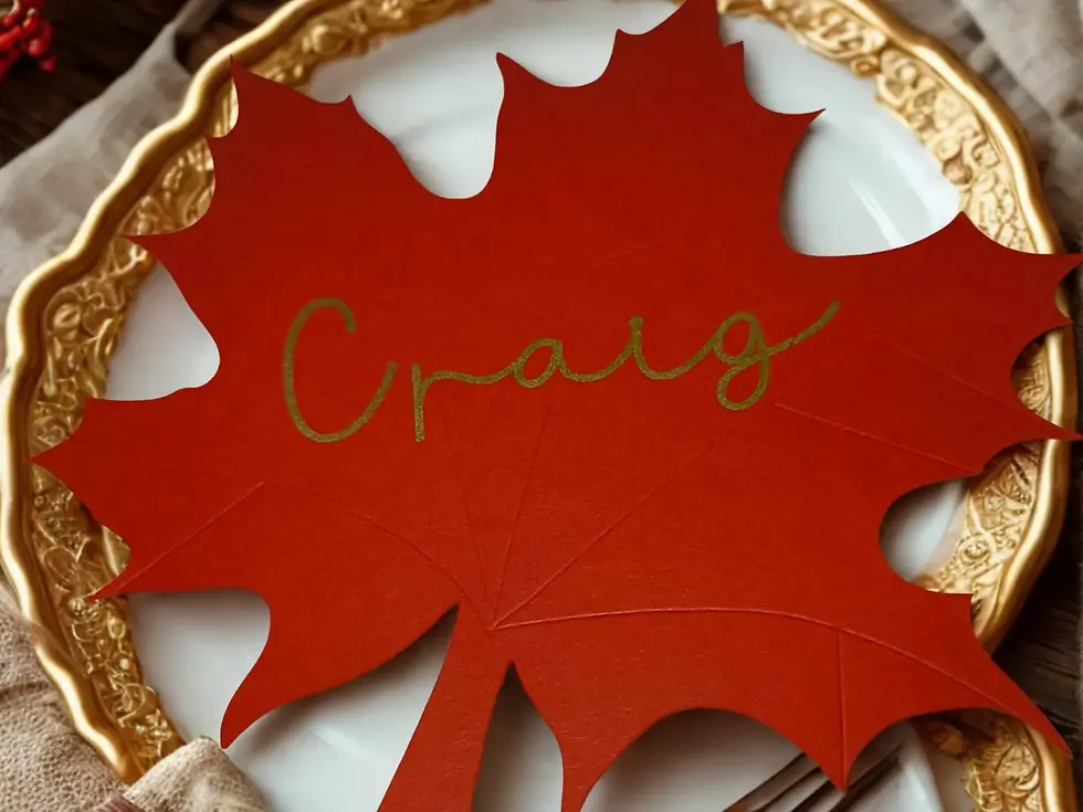 Thumbnail: Close-up of a deep red maple leaf place card with "Craig" in gold calligraphy on a decorative gold-rimmed plate.
