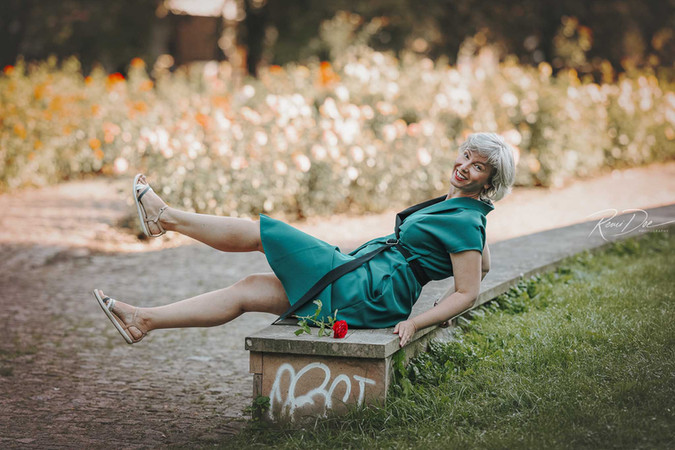 žena se šedými vlasy v zelených šatech leží na lavičce v parku Stromovka Praha