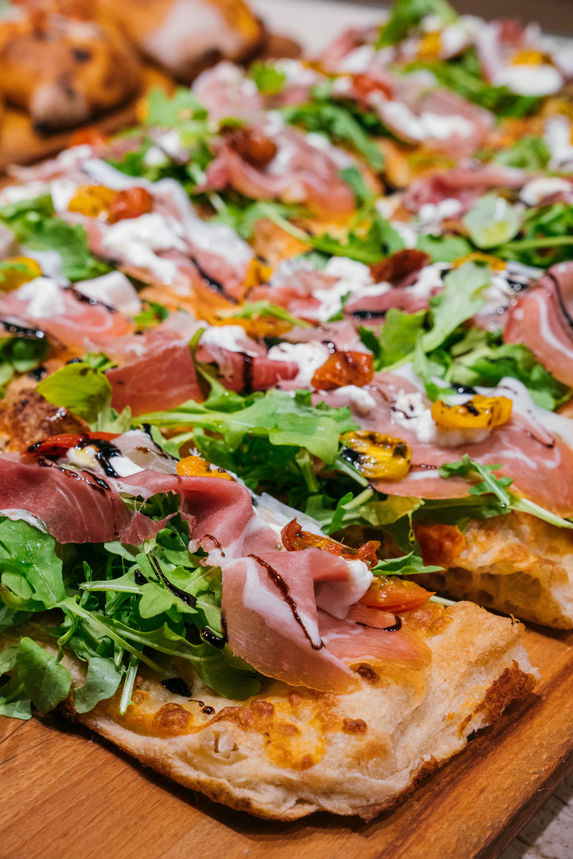 Prosciutto and rocket flatbread pizza served fresh on a restaurant table.