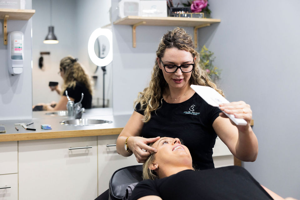 Client reviewing pre-drawn brows before cosmetic tattoo at our Noosa clinic