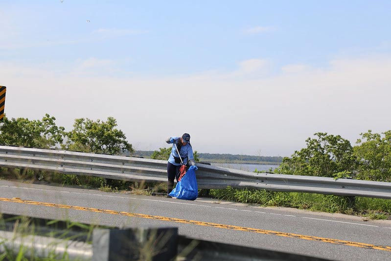 A volunteer picking up trash near the road during  Waterway Cleanup