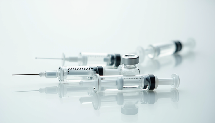 Close-up view of a syringe with dermal filler and Botox vials on a clean surface