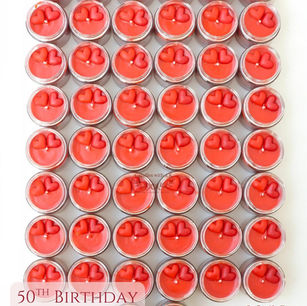 A massive, clean top-down grid layout of dozens of red heart glass candles with a text overlay that reads "50th Birthday Return Gifts."