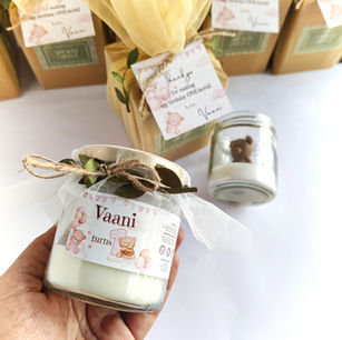 Close-up of a personalized 1st birthday favor jar candle featuring a custom "Vaani turns 1" label, delicate white tulle ribbon, and a rustic jute twine bow.