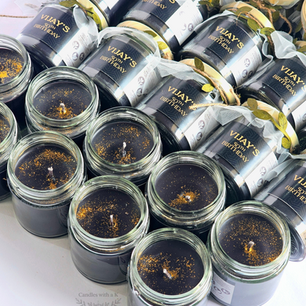 High-angle close-up view of a bulk custom event order featuring black soy wax jar candles delicately dusted with shimmering gold glitter.