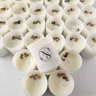 A top-down grid layout of bulk white frosted glass candles topped with tiny natural seashells, featuring a central candle with a personalized "NS" monogram and event date label.