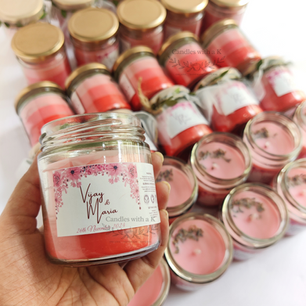 Close-up of a hand holding a personalized 200ml soy wax jar candle featuring a pink floral custom label for Vijay and Maria's anniversary celebration.