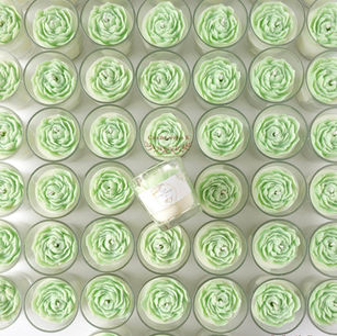 Top view of handmade sage green peony flower soy wax votive candles in clear glass jars arranged in a grid, with one personalized communion sticker jar at center, by Candles with a K Bangalore