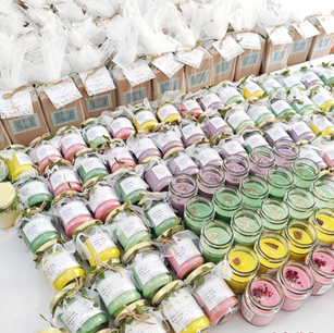 Bulk rows of personalized memorial return gift candles in pastel colors with "In Loving Memory" labels, alongside wrapped remembrance gift boxes