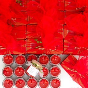 An overhead flat lay of red soy candles with 3D heart embeds next to rows of custom gift boxes elegantly wrapped in vibrant red tulle netting.