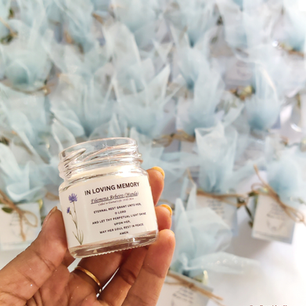 Hand holding a personalized "In Loving Memory" candle jar for Filomena Rebeiro with a floral design and remembrance prayer text