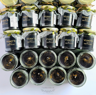 Grid display of custom "Vijay's 50th Birthday" favor candles showcasing elegant geometric black labels and smooth black wax topped with brilliant golden glitter