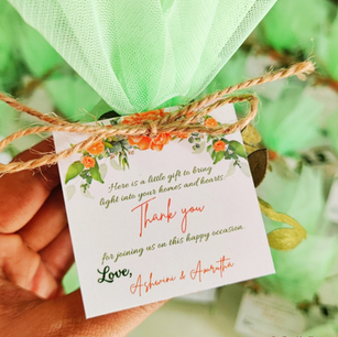 Hand holding a personalized 40th birthday return gift candle, with pink net-wrapped favors blurred in the background