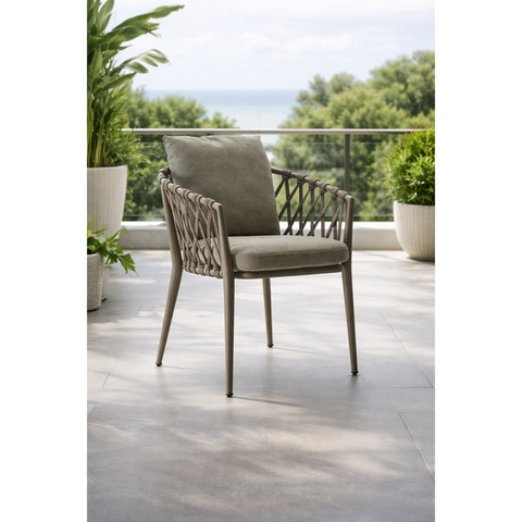 Woven outdoor armchair with grey cushion on a balcony overlooking the sea.