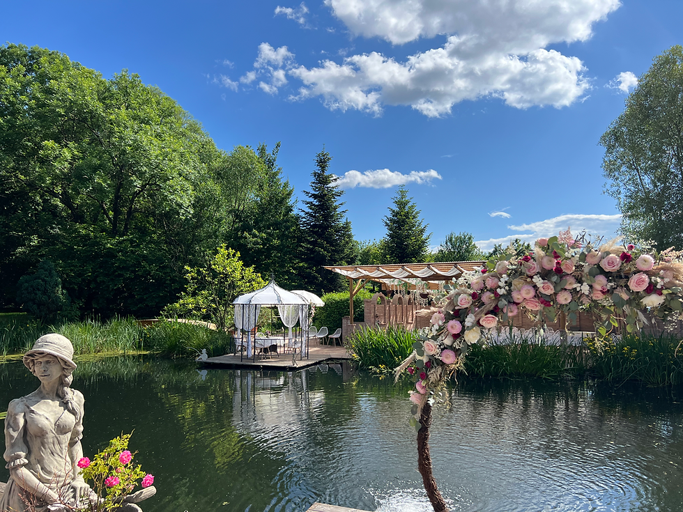 Teich mit Pavilion, Blumenkranz und einer Statue eines Mädchens beim Weingut Kolleritsch. Strahlend blauer Himmel und nur wenige Wolken.