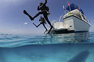 under-view-showing-divers-performing-giant-stride-entry-into-the-clear-calm-waters-of-the.