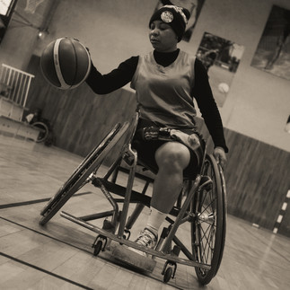 Une femme en fauteuil roulant dribble un ballon de basket sur le terrain, démontrant sa détermination et son talent