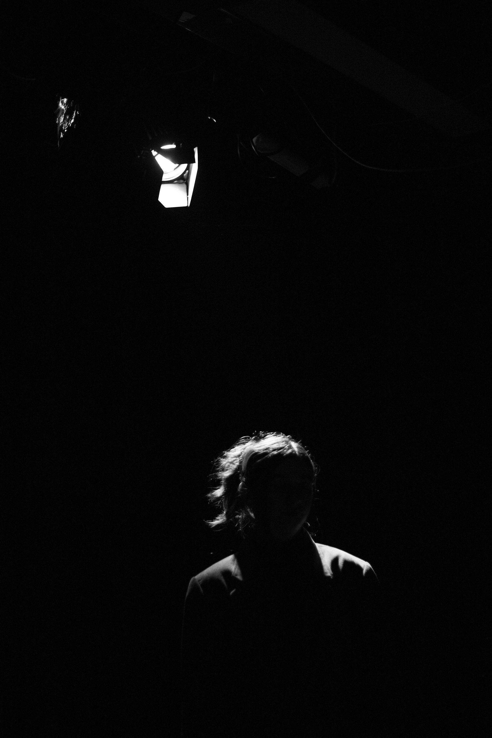 Photo en mode portrait noir et blanc. En bas de l'image la mannequin, on voit que ça silouhette et en haut de l'image le projecteur lumineux qui l'éclaire de dos