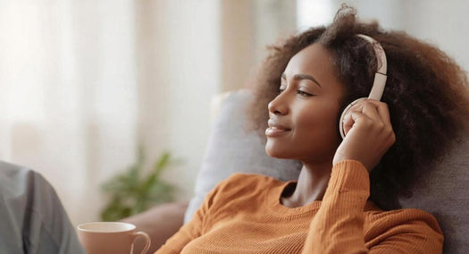 African american woman relaxing with tea and listening to music through headphones