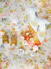 White bridal shoes, perfume, and jewelry on floral fabric
