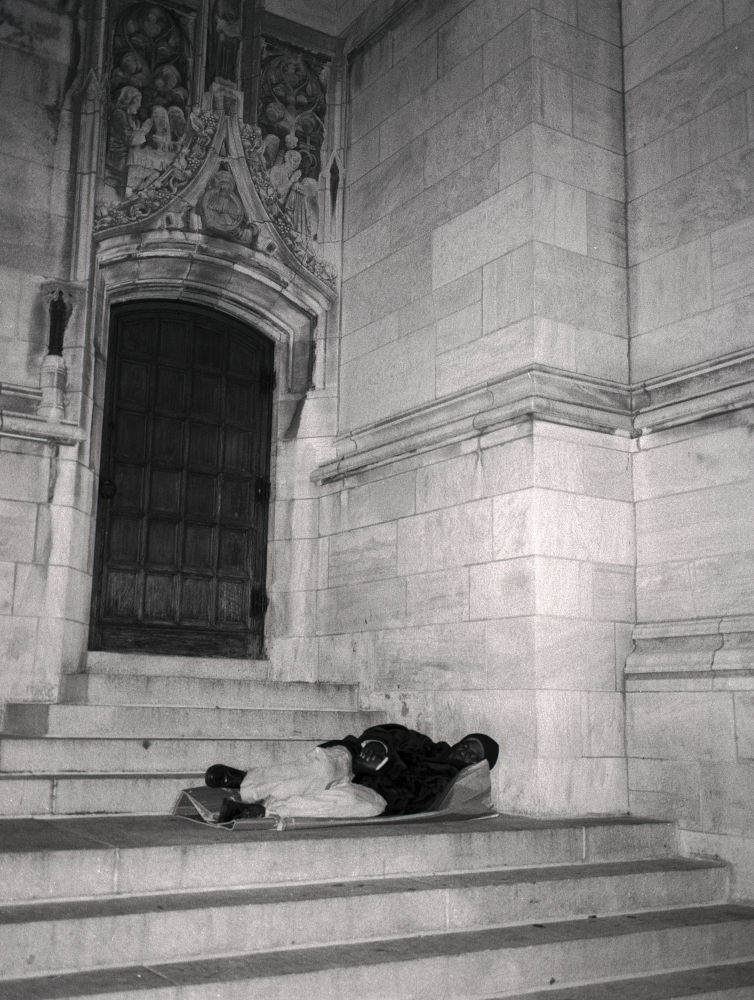 photographie en noir et blanc argentique, vintage.  Un homme  sans abri (homeless) dort sous le fronton d'une église de New York, indifférent à la victoire de Barack Obama 2008  quelques minutes plus tôt. 